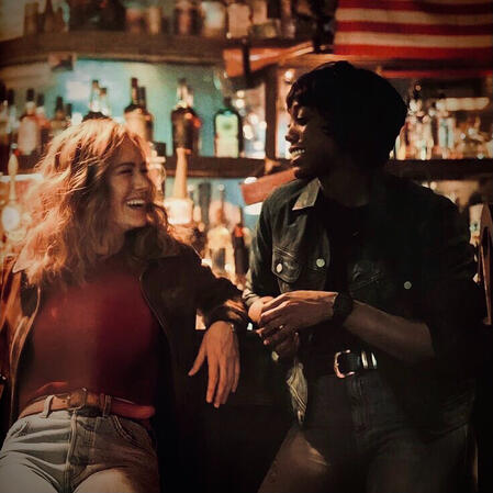 click this image for an mcu quote. the image shows carol danvers and maria at panchos, leaning against at table and smiling at each other.